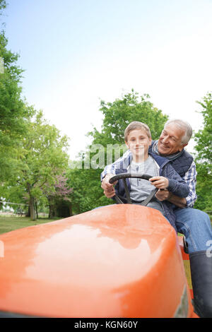 Senior man with grandkid riding on lawnmower Stock Photo