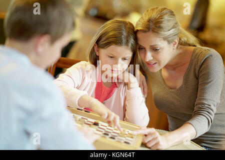 Mother with kids playing checkers at home Stock Photo