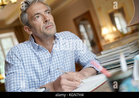 Mature man sitting at desk writing on notebook Stock Photo