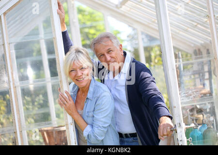 Senior couple standing by greenhouse in garden Stock Photo