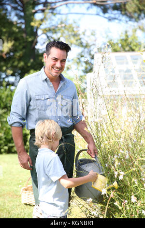 Father and son watering plants in garden Stock Photo