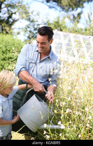 Father and son watering plants in garden Stock Photo