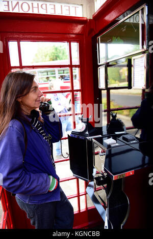 Female local resident using a traditional red phone box which has been converted into a small visitors centre. The interior of the phone box now has a Stock Photo