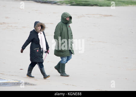 Dog walkers braving the cold windy conditions walking along the sandy shoreline and beach at New Brighton on Merseyside, England, UK Stock Photo