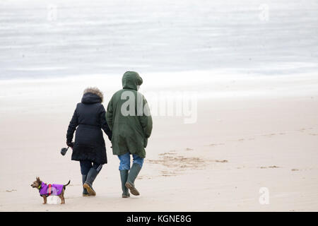 Dog walkers bravingn the cold windy conditions walking along the sandy shoreline and beach at New Brighton on Merseyside, England, UK Stock Photo