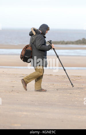 New Brighton Wirral, 9th November 2017. UK Weather. Windy, showery weather passing over from the west today to leave a bright afternoon but with increasing winds. A photographer heading to the beach as the sands whip up and dressed for the cold windy condtions at New Brighton Stock Photo