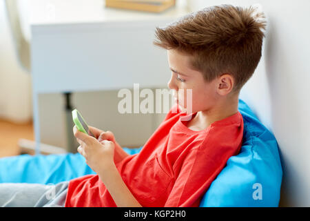 boy with smartphone lying on bed at home Stock Photo