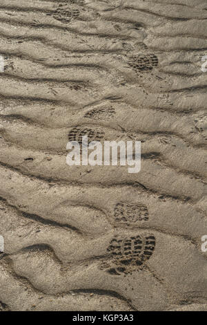 Trail of footprints in the wet rippled sand of a Cornish beach. Leave no trace metaphor. Stock Photo