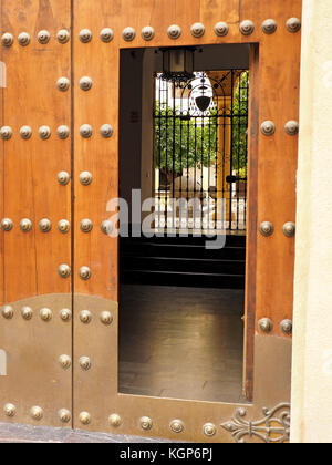 open standard doorway within large historic studded wooden door giving view into hall & courtyard with sculpture steps and pillar in Córdoba, Spain Stock Photo