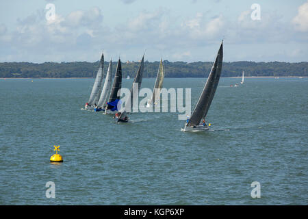 Yacht's racing on a summers day in the Solent off the Isle of Wight. Colourful sails and hulls against a green sea. Good windy weather for a race. Stock Photo