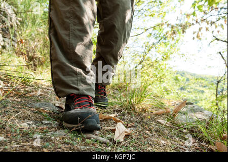 Hiking shoes with red laces and legs wearing long brown trousers of an hiker walking on a path in the wood Stock Photo