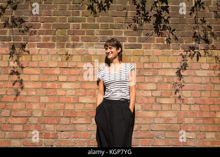 Young Woman dressed in urban minimal style with black and white striped T-shirt and black trousers. Brick wall as background Stock Photo
