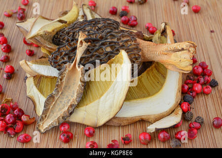 Mixed dried first class quality Cep and Morel mushrooms on dark bamboo wooden background, with lot of red pepper grains Stock Photo