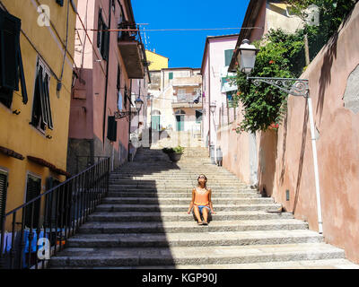 Young woman with sunglasses dressed in casual summer clothes enjoying the sun in an alley of a small rural medieval village in Italy Stock Photo