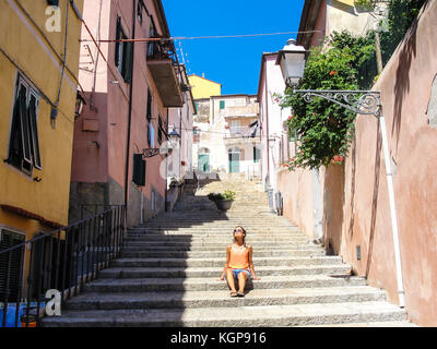 Young woman with sunglasses dressed in casual summer clothes enjoying the sun in an alley of a small rural medieval village in Italy Stock Photo