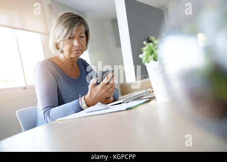 Senior woman working in office using smartphone Stock Photo