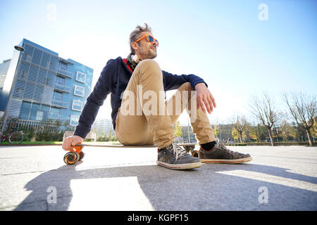 Trendy urban guy sitting on skateboard in park Stock Photo