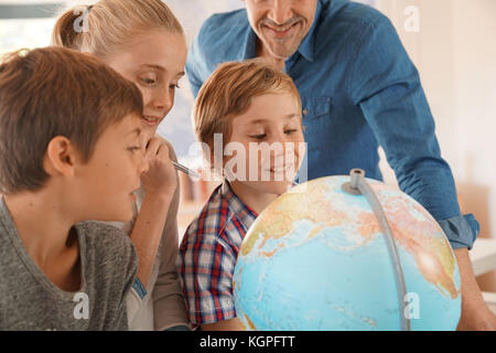 Teacher with kids in geography class looking at globe Stock Photo