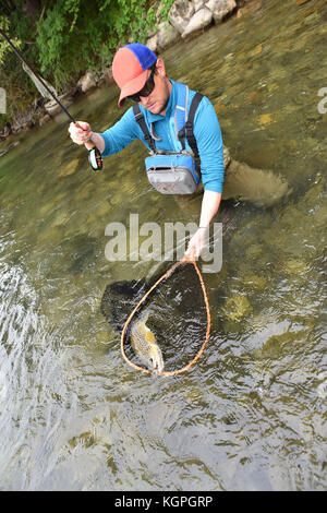 Fly fisherman catching brown trout in river Stock Photo