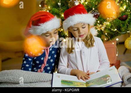 Kids reading book by Christmas tree Stock Photo