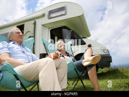 Senior couple relaxing in camping folding chairs, camper in background Stock Photo