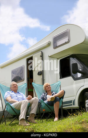 Senior couple relaxing in camping folding chairs, camper in background Stock Photo