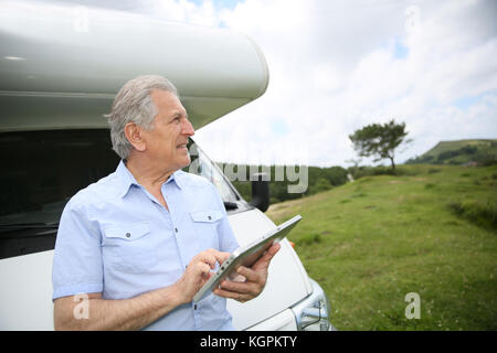 Senior man by camper websurfing on digital tablet Stock Photo
