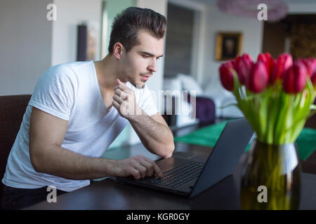 Young casual caucasian man surfing on internet by laptop indoors Stock Photo