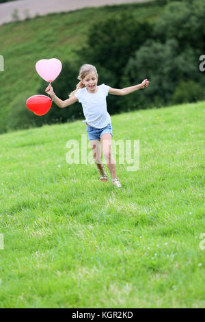 Little girl running in field with balloons in one hand Stock Photo