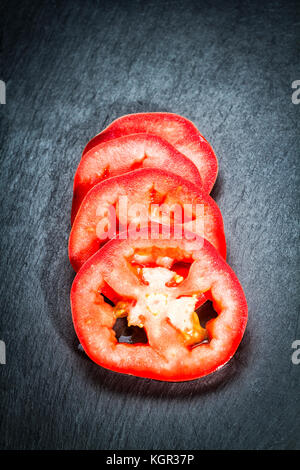 Tomato slices (Solanum lycopersicum) on a black slate board. Stock Photo