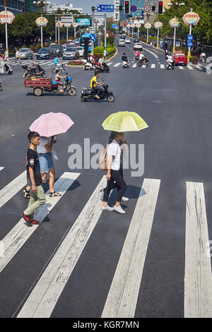 Guilin, China - September 15, 2017: Women with sun umbrellas cross street in downtown Guilin. Stock Photo