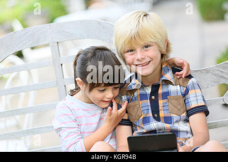 Kids sitting on outdoor bench and playing video games Stock Photo