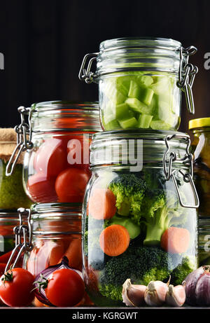 Jars with marinated food and organic raw vegetables. Stock Photo