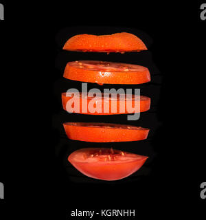 Flying tomato. Sliced red tomato isolated on black background. Levity vegetable floating in the air Stock Photo