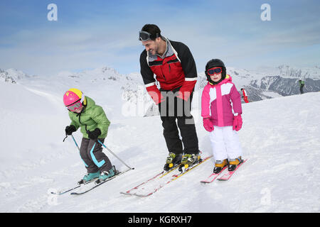 Ski teacher helping young kids to go down ski slope Stock Photo