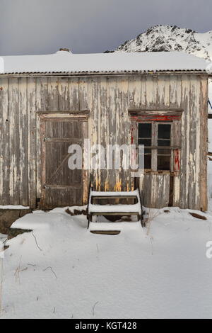Snow covered fully ruined-abandoned-paint faded wooden hut with stair leaning on the wall-foot of snow capped mount Hustinden beside E10 European road Stock Photo