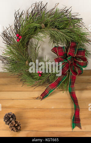 A beautiful handmade bow of red, green, and gold trimmed ribbon on a twig wreath with white pine boughs. pine cones, and red berries along with two pi Stock Photo