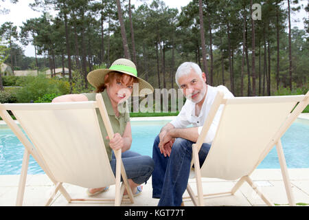 Senior couple sitting in deckchairs by a pool Stock Photo
