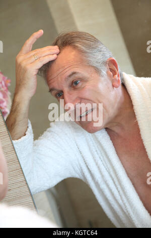 Senior man looking at hair in mirror Stock Photo