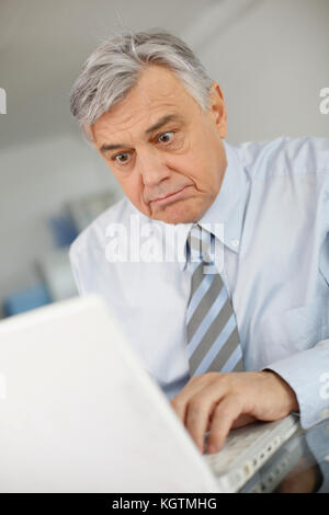 Senior businessman working on laptop with surprised look Stock Photo