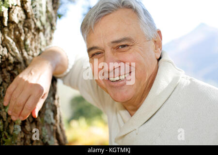Portrait of smiling senior man leaning against tree Stock Photo