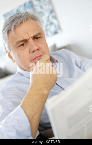 Senior man reading newspaper with puzzled look Stock Photo