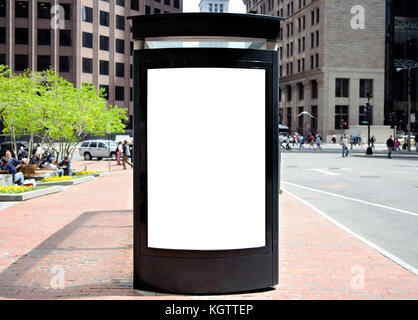 Bus shelter advertising. Frontal view of blank billboard in American city. Brick sidewalk, springtime. Office buildings and people in background. Stock Photo