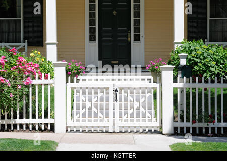 White gate and picket fence with climbing roses, frontal view, Porch steps and house facade in background Stock Photo