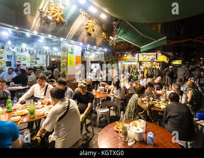 HONG KONG, CHINA - JUNE 16, 2017: Tourists and local dine in a restaurant in the streets of Kowloon near the famous Temple night market in Hong Kong. Stock Photo