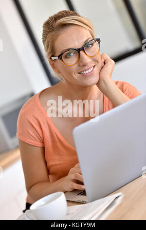 Blond woman with eyeglasses working from home with laptop