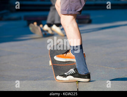 Skateboarding - detail of skateboard and legs with trainers. Stock Photo
