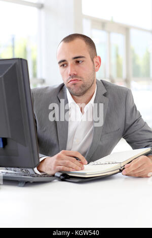 Businessman writing on agenda with bored look Stock Photo