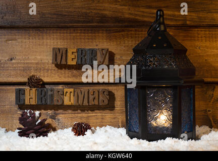 Merry Christmas text on a wooden background with burning lantern on snow Stock Photo