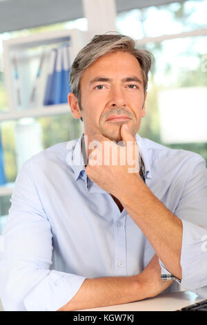 Thoughtful worker in office with hand on chin Stock Photo